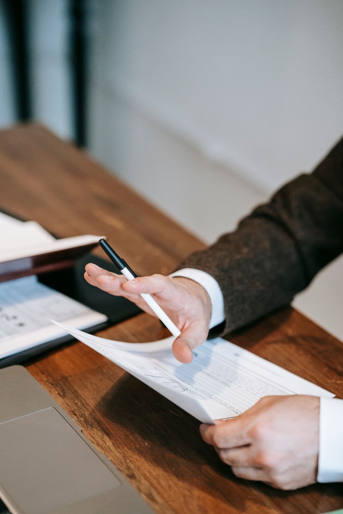 A hand holding a pen over financial documents on a wooden desk
