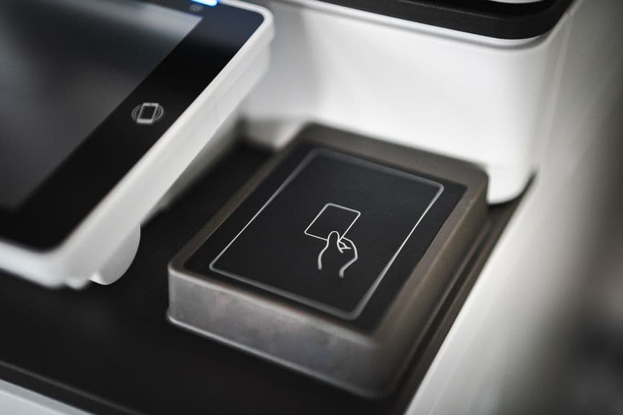 A hand using a card at a payment terminal beside a laptop