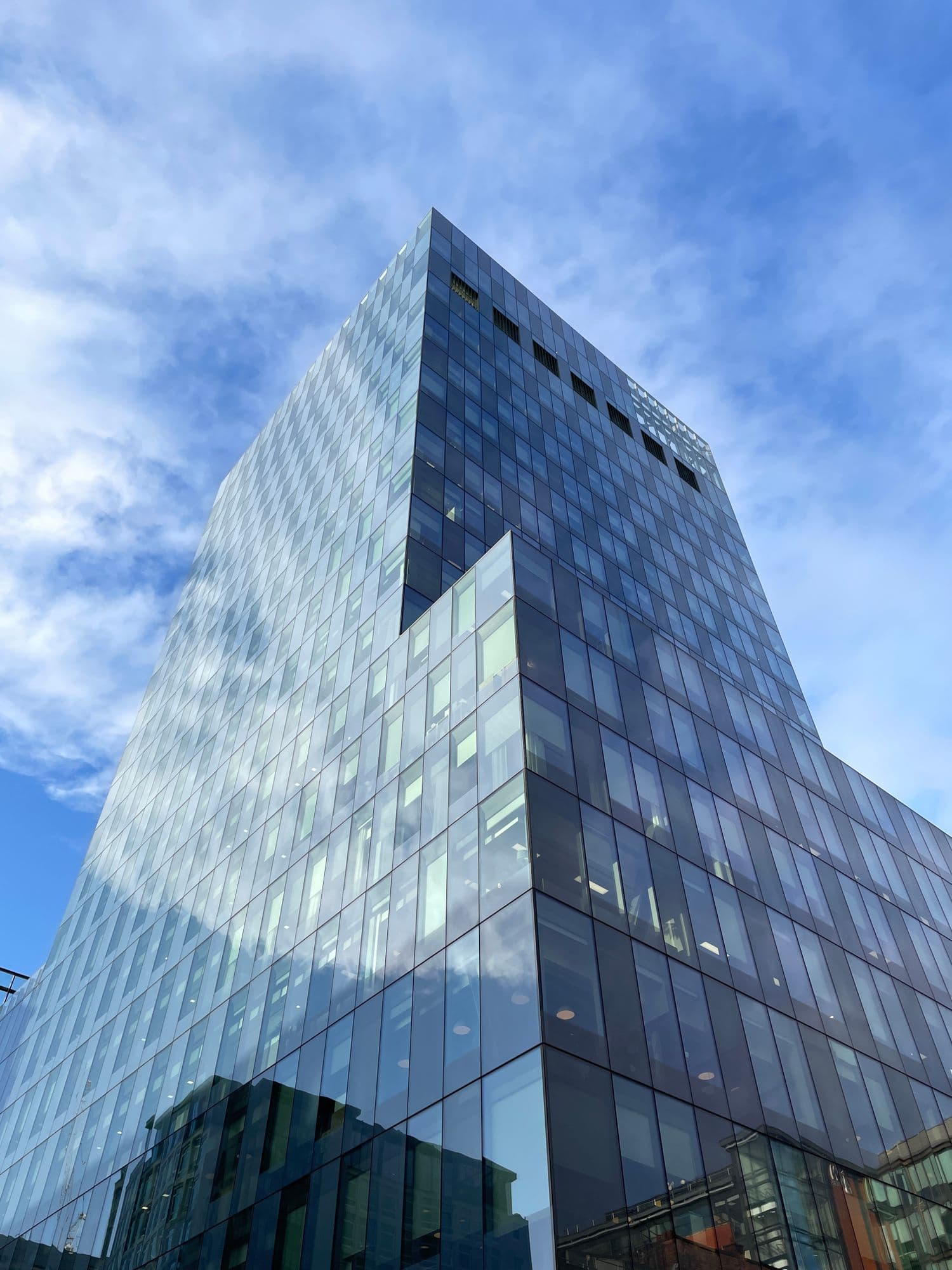 Upward view of a glass office tower against a partly cloudy sky