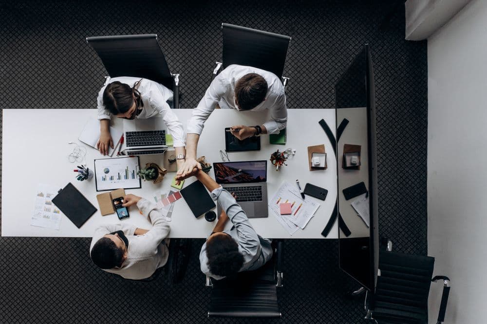 Overhead view of a team working at a boardroom table with laptops and papers