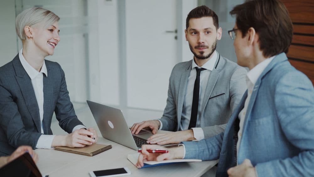 A team of professionals discussing plans around a table with laptops